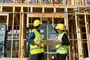alt="Two people wearing hard hats checking a building construction site"