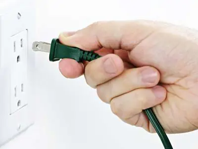 Photo of a hand plugging a black cord into a wall socket